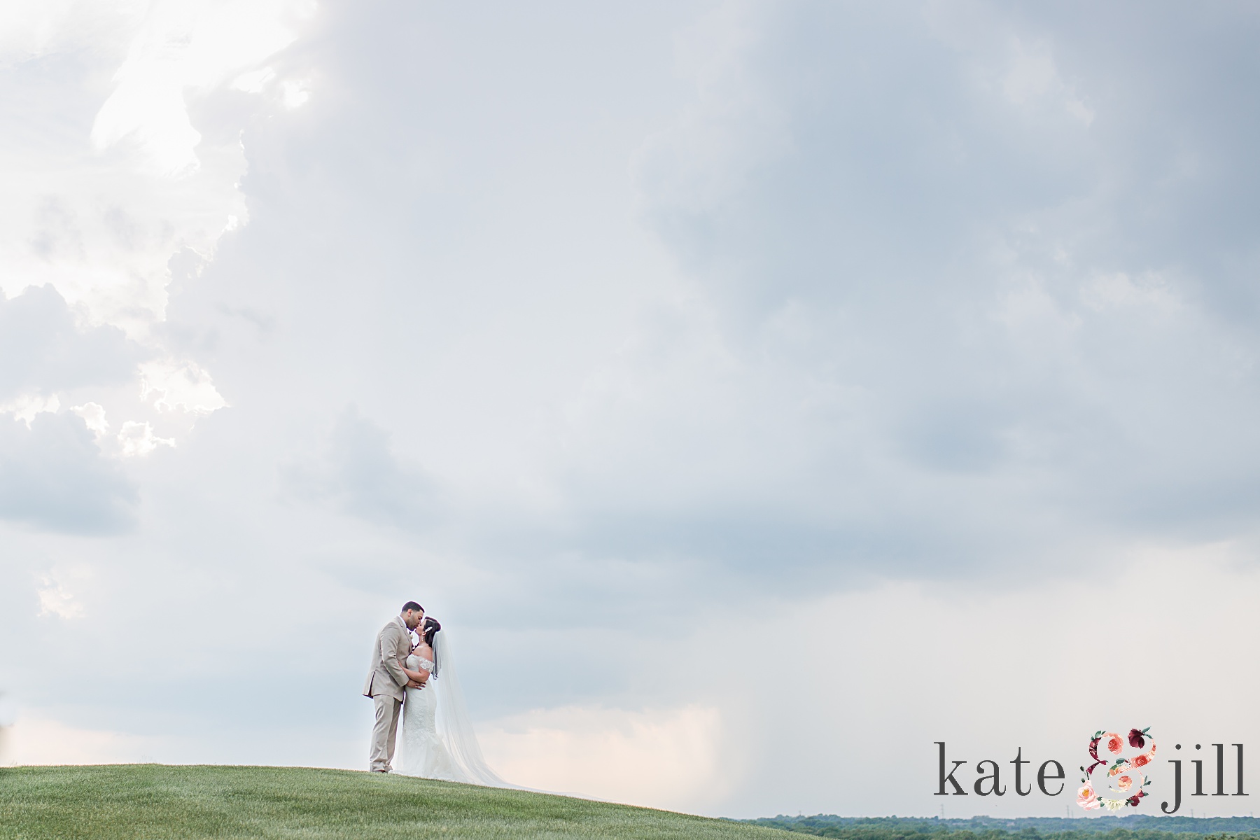 bride and groom kissing on hill before storm