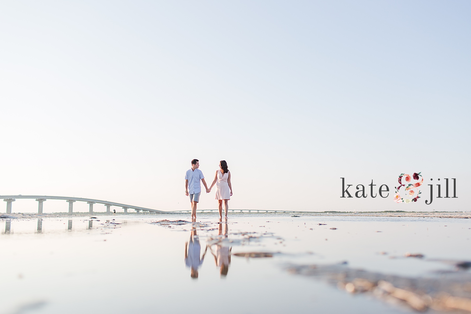 couple standing in water in front of bridge ocean city engagement photos