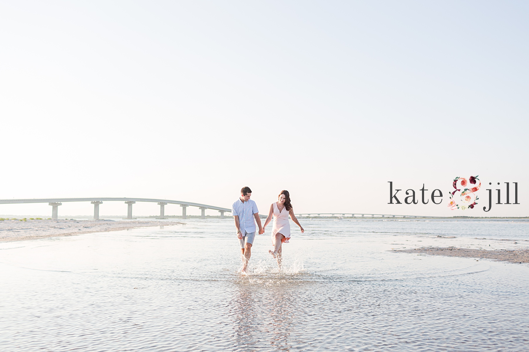 couple running in water in front of bridge ocean city engagement photos