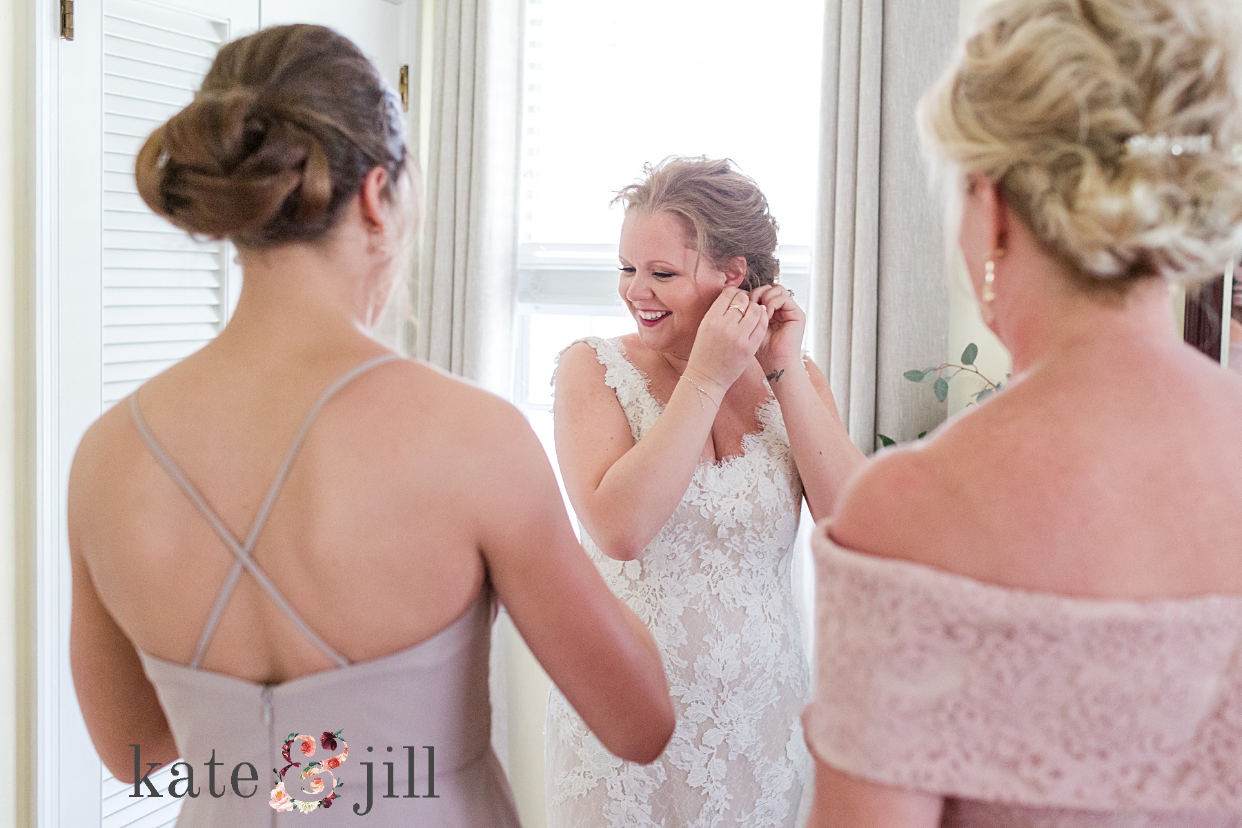 bride putting in her earrings while mom and sister watch
